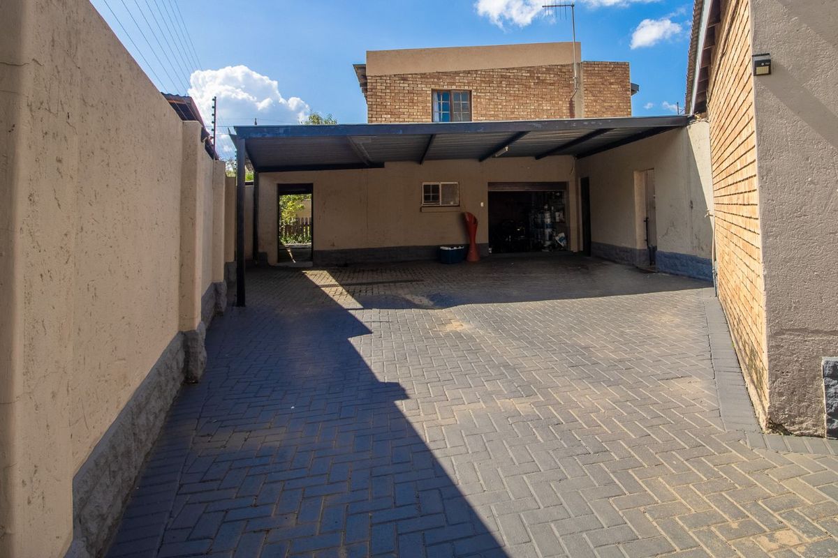 A paved driveway area featuring a covered carport structure and access to a garage, enclosed by high boundary walls.