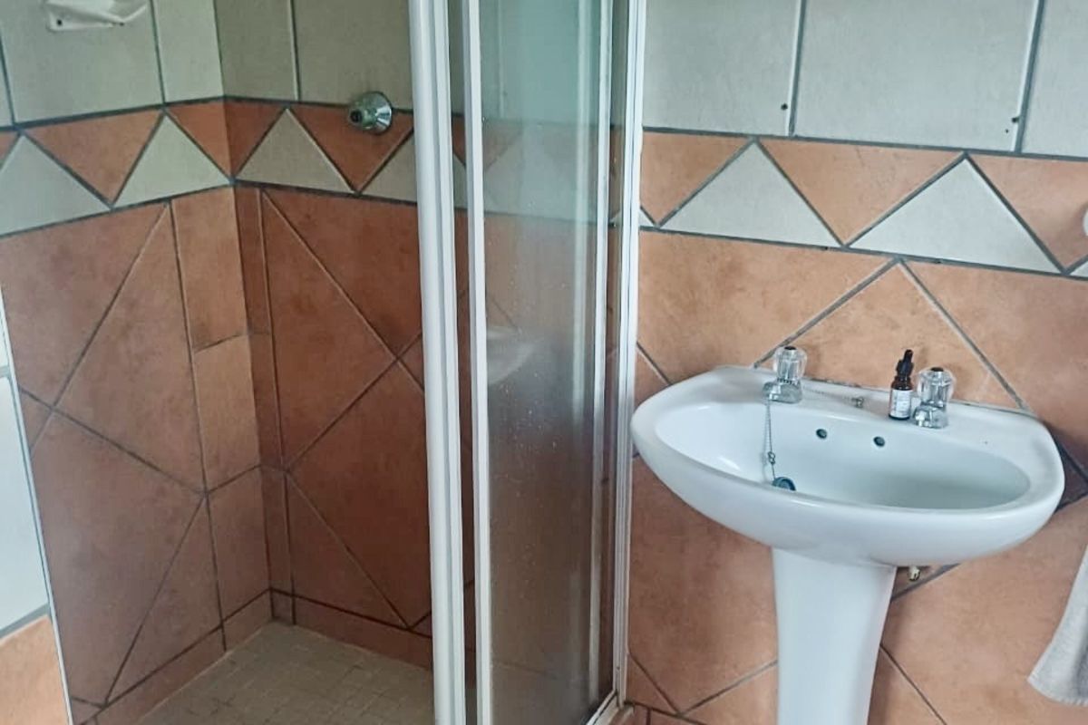 A compact bathroom featuring a shower enclosure with glass doors and a white pedestal basin with wall-mounted mirror.