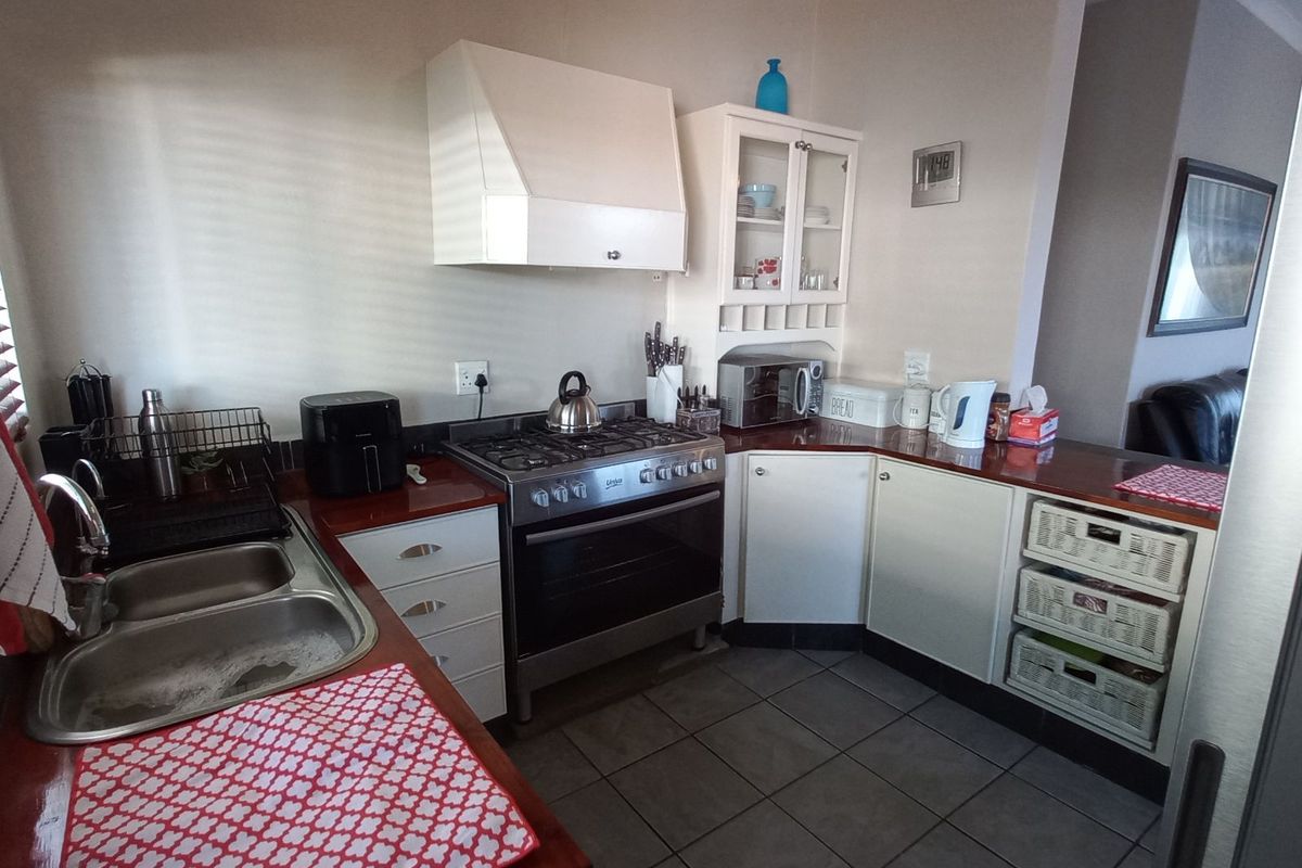 A functional kitchen featuring wooden countertops, a gas stove with extractor fan, stainless steel double sink, and tiled flooring.
