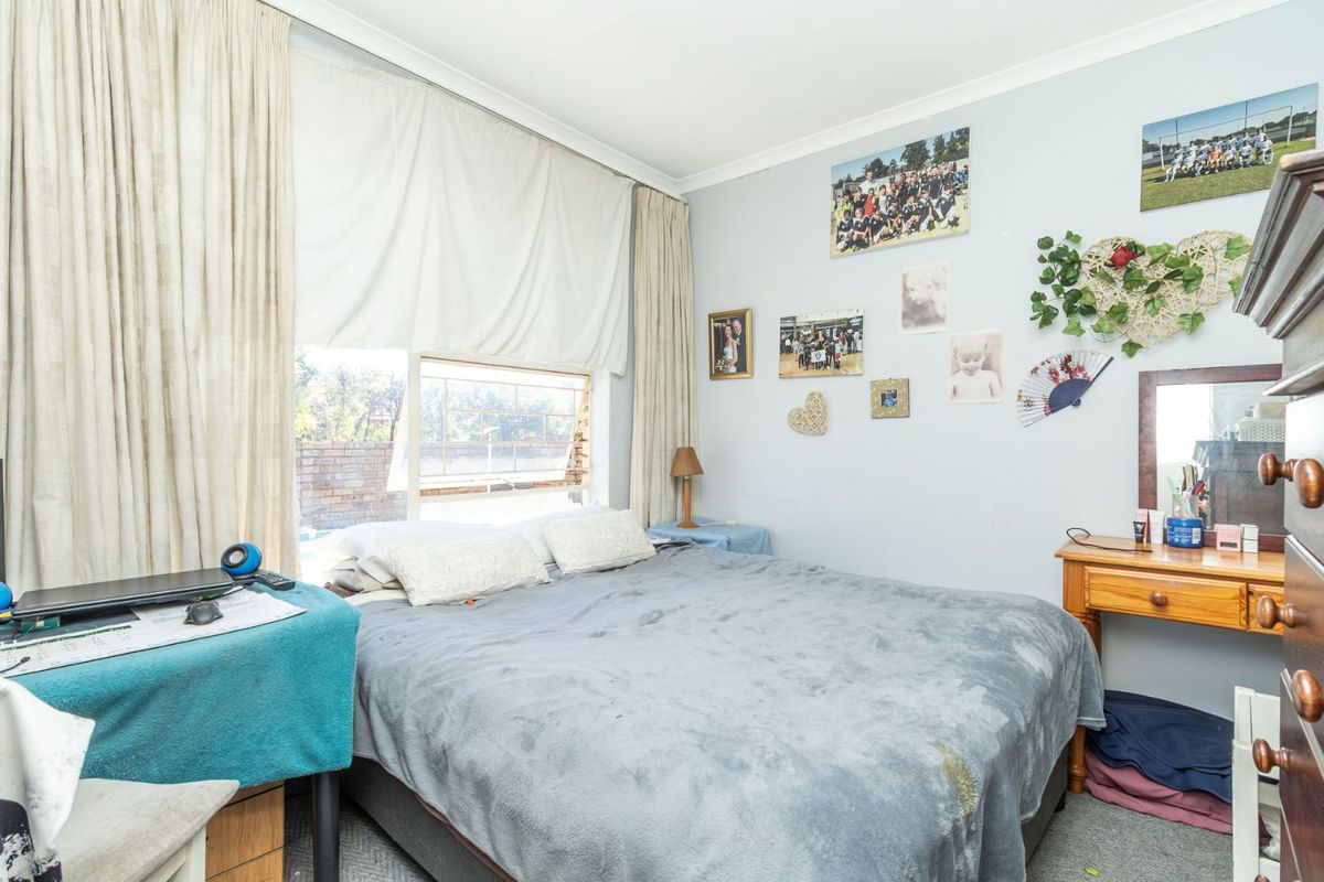 A standard bedroom featuring a large window with curtains, providing natural light and a view of the exterior brick wall.