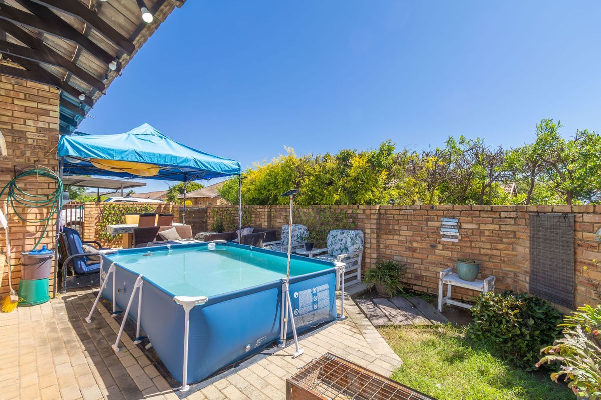 A rear garden area featuring a paved patio, brick boundary walls, and a portable above-ground swimming pool.