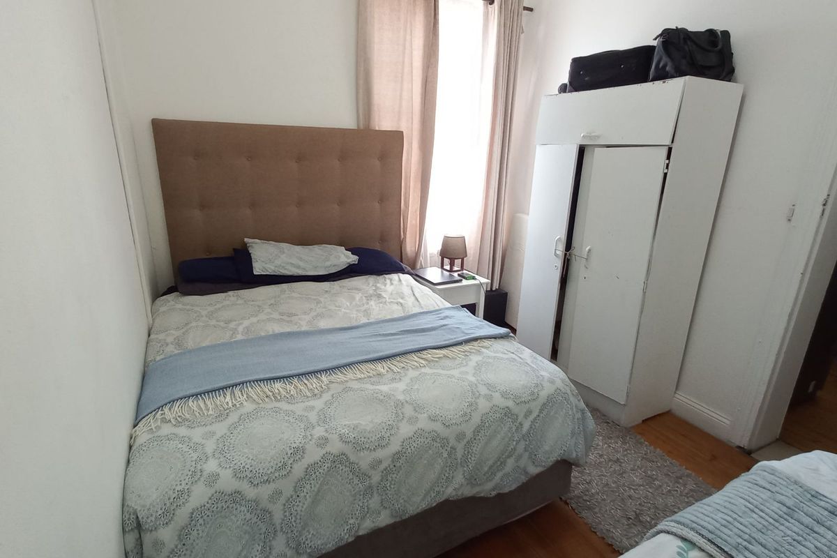 A compact bedroom featuring timber flooring, a window with curtain rod, and built-in wardrobe space.