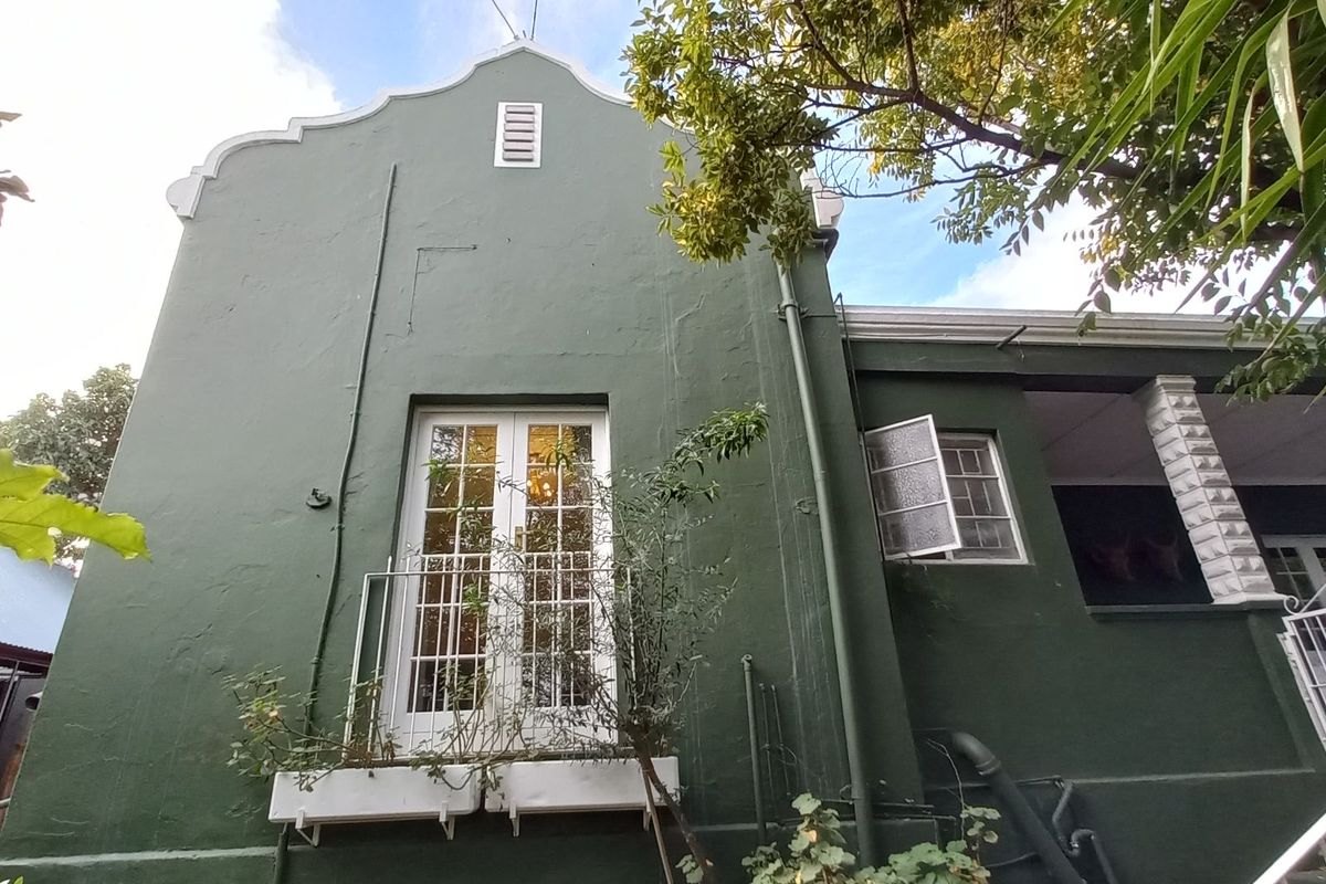 Rear exterior view of the property featuring a green facade, white-framed French doors with a small balcony, and a covered patio area.
