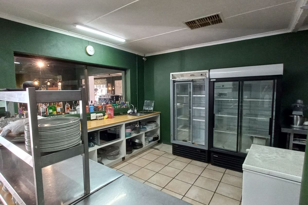 A functional commercial kitchen area featuring stainless steel prep counters, built-in shelving, and commercial-grade glass-door refrigeration units.