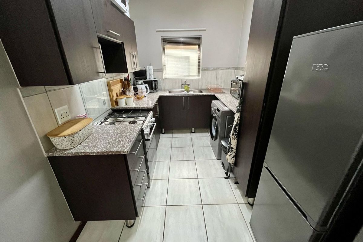 Compact kitchen featuring dark cabinetry, granite-look countertops, tiled flooring, a built-in gas hob, and an integrated laundry space.