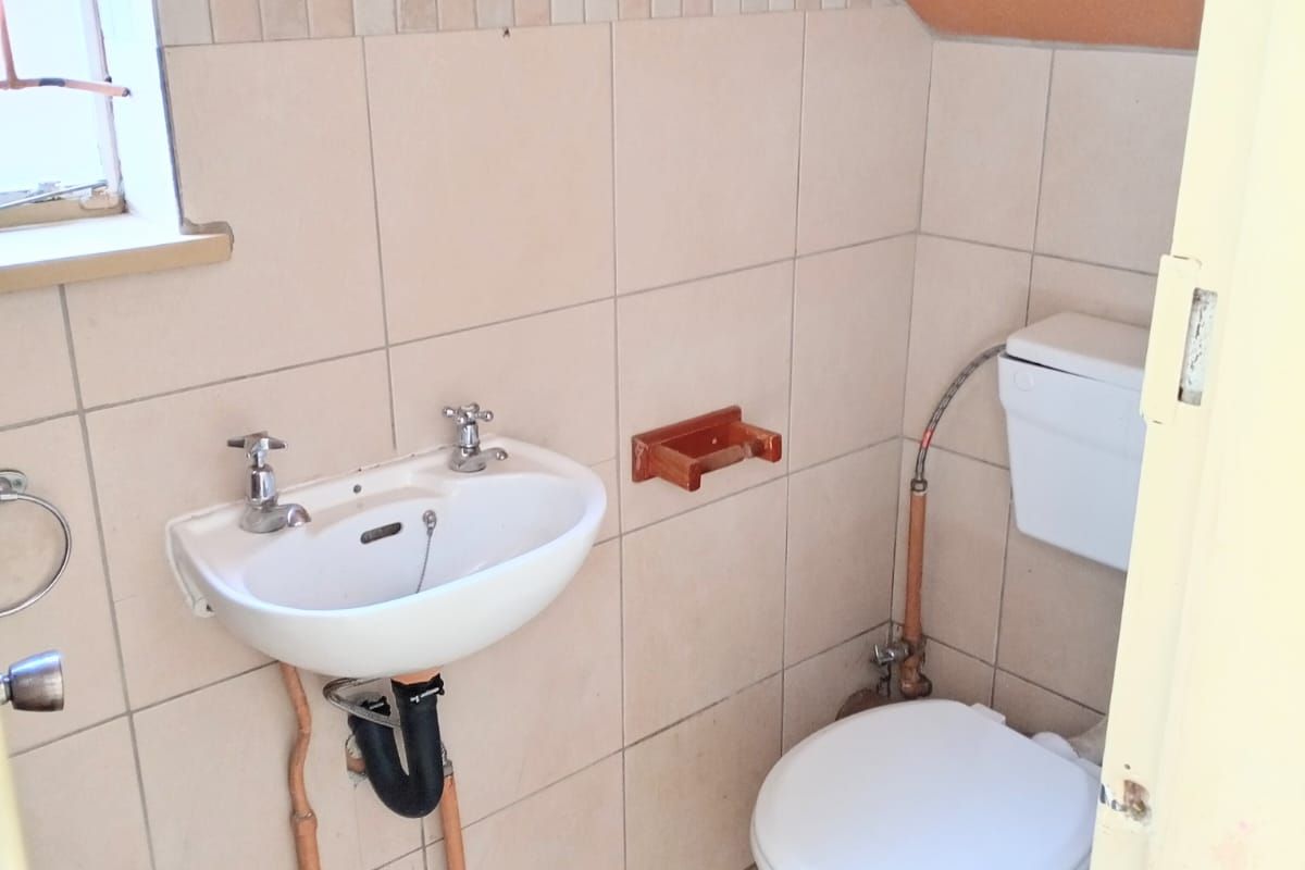 A compact guest bathroom featuring a wall-mounted basin and toilet, finished with neutral wall tiles and a sloped ceiling.