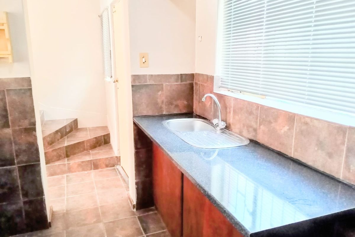 A functional kitchen area featuring dark stone countertops, a stainless steel sink, and tiled splashbacks, leading to a staircase.