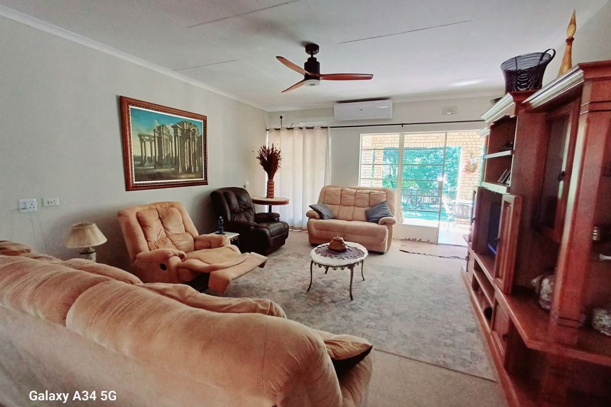 Spacious living room featuring a ceiling fan, wall-mounted air conditioning unit, and sliding glass doors providing access to the outdoor patio area.