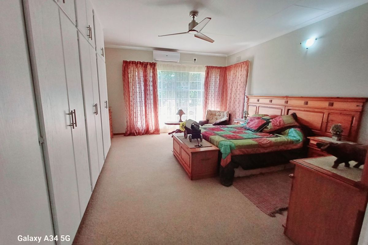 Spacious bedroom featuring extensive built-in cabinetry, a ceiling fan, and wall-mounted air conditioning unit, providing comfortable climate control and ample storage space.