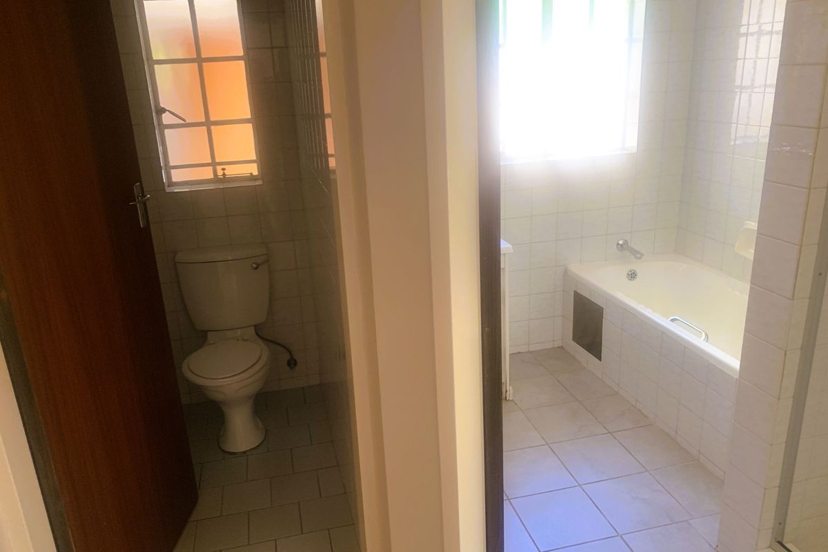 A functional bathroom featuring a separate toilet area, a built-in bathtub, and tiled finishes throughout.