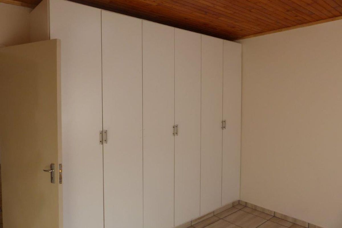 A bedroom featuring floor-to-ceiling built-in cupboards, tiled flooring, and a timber-paneled ceiling.