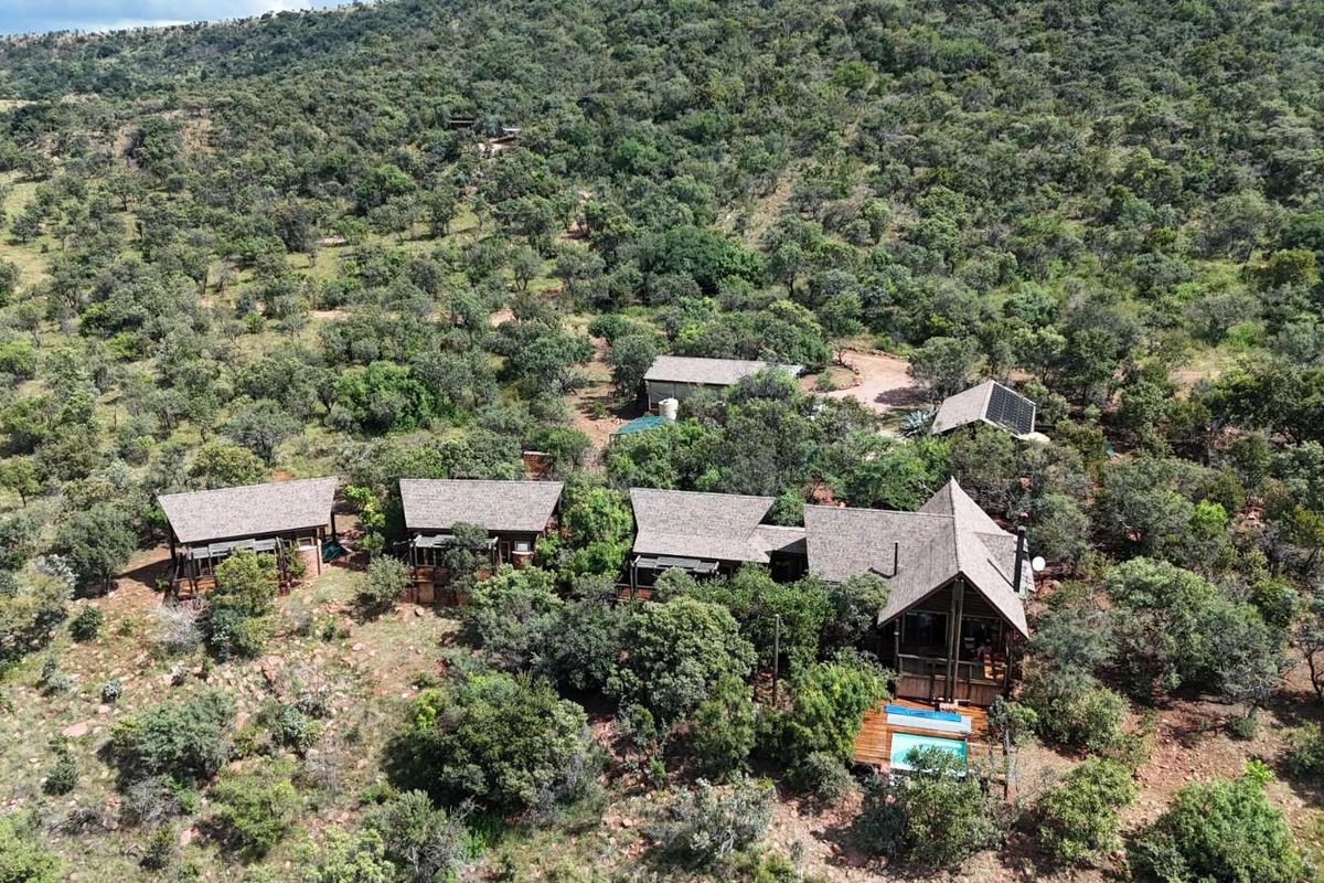 Aerial view of a secluded bushveld property featuring multiple detached structures with pitched roofs, integrated decking, and a private swimming pool.