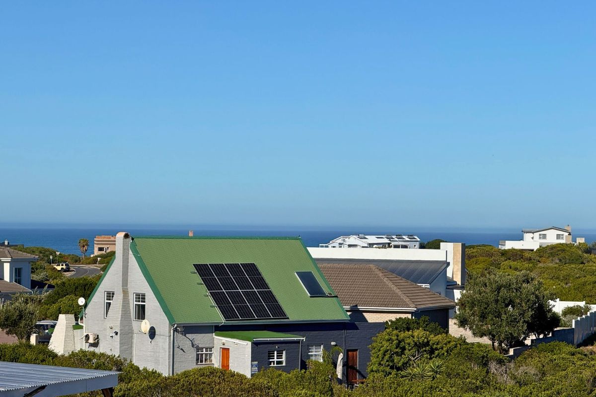 An elevated view of a residential property featuring a green metal roof with integrated solar panels, set within a coastal landscape.