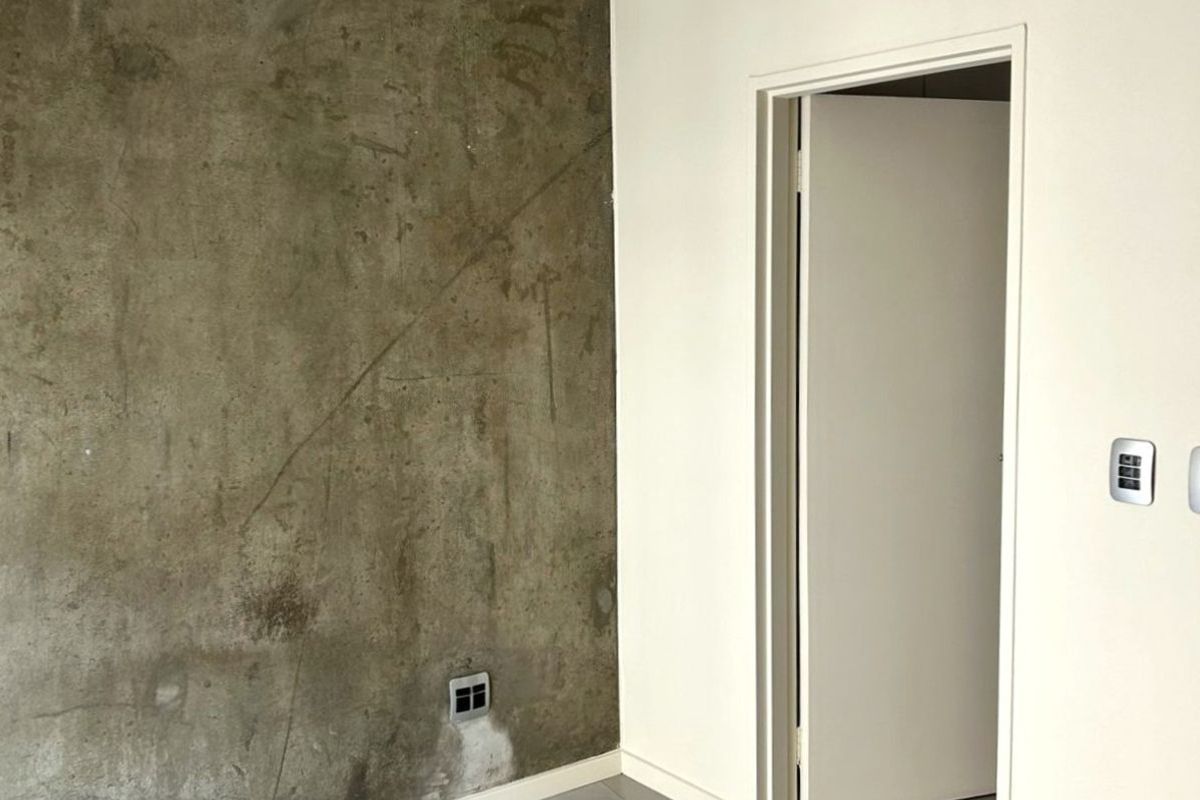 A minimalist room featuring large format grey floor tiles, a textured concrete feature wall, and a clean white door frame.