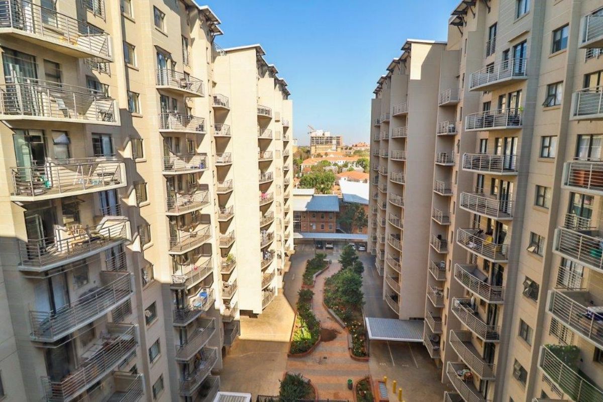 An elevated view of the apartment complex courtyard, featuring landscaped pathways, paved areas, and multiple residential balconies overlooking the central outdoor space.