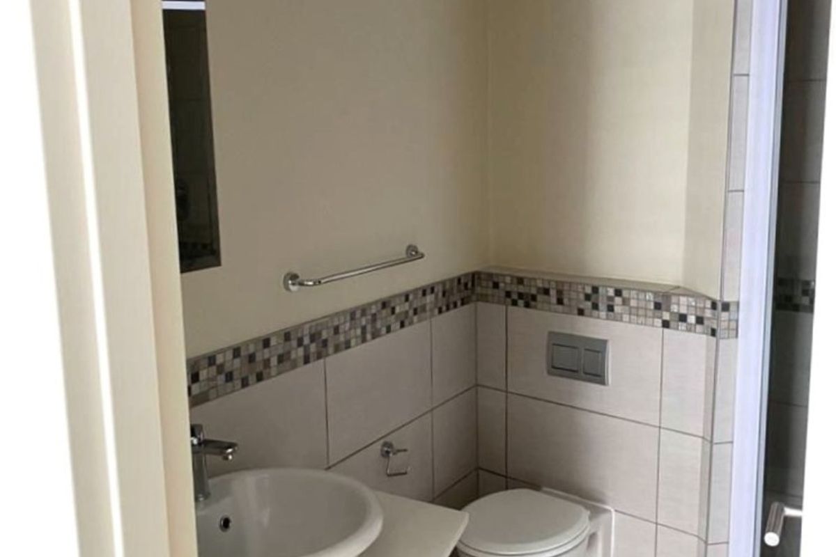 A compact bathroom featuring a modern vanity with a vessel sink, a wall-mounted toilet, and a tiled shower enclosure with an extractor fan.