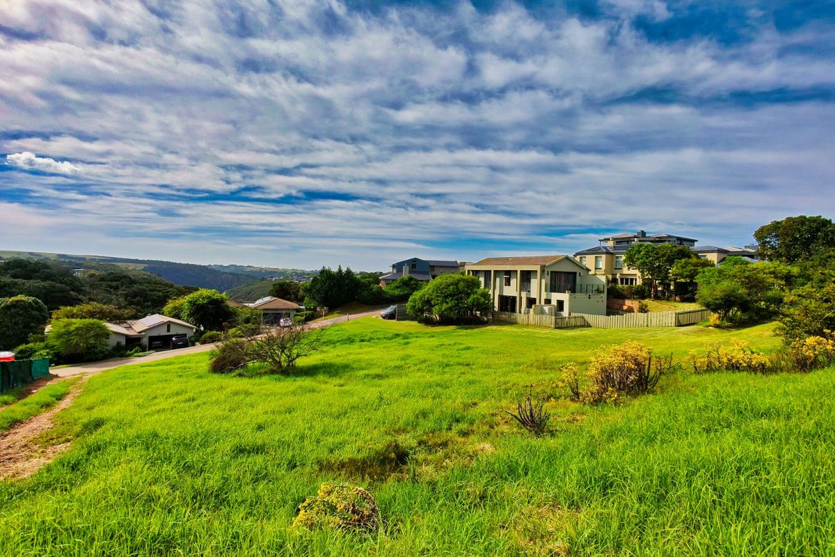 A scenic view of a vacant residential plot featuring lush green grass, overlooking the surrounding neighbourhood and distant landscape.