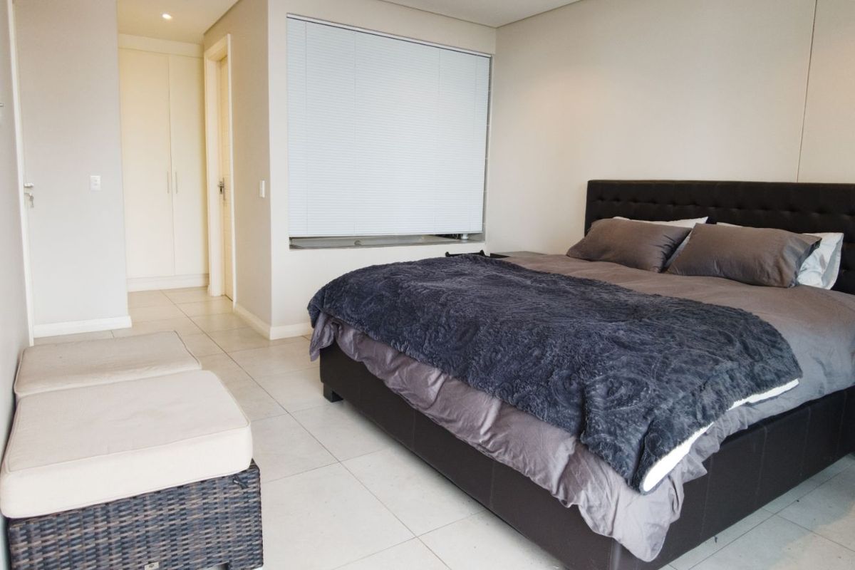 A spacious bedroom featuring neutral tiled flooring, built-in cupboards, and a window fitted with white venetian blinds.