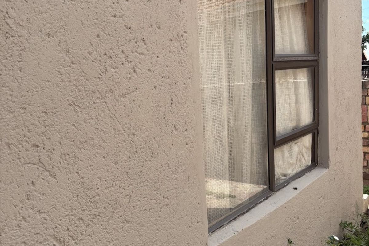 A side view of the property exterior featuring a textured wall finish and a dark-framed window.