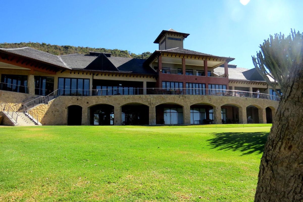 A view of the rear elevation of a large residential property featuring stone-clad arches, expansive balconies, and well-maintained landscaped grounds.