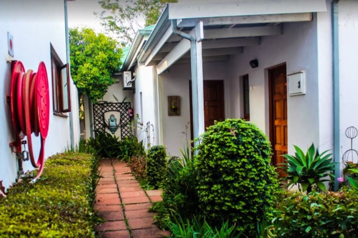 A paved exterior walkway leading to building entrances, featuring a fire hose reel, covered porch area, and established garden landscaping.