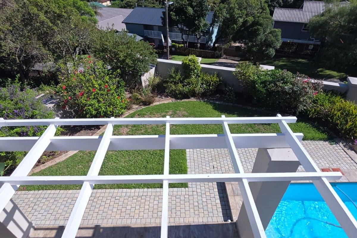 Elevated view of a private backyard featuring a swimming pool, paved patio area, and a white timber pergola structure.