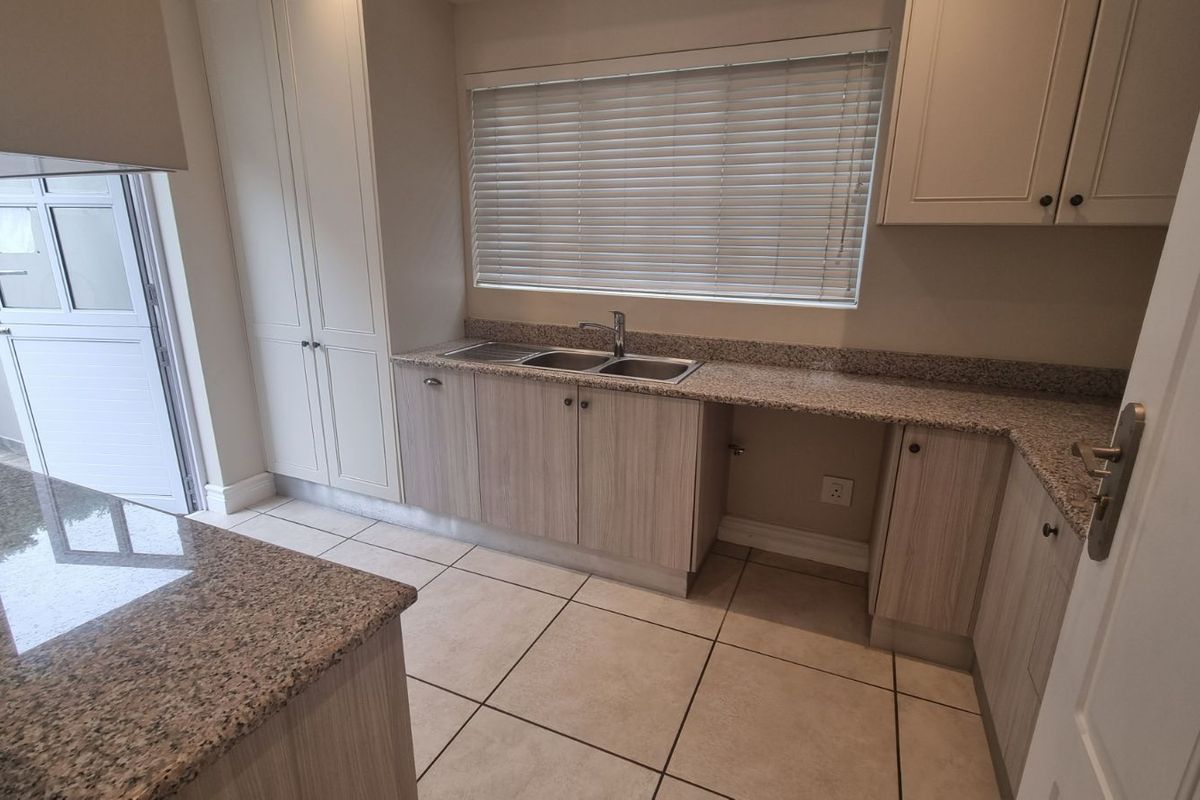 A functional kitchen featuring granite countertops, light wood-finish cabinetry, tiled flooring, and a double-basin sink with a window view.