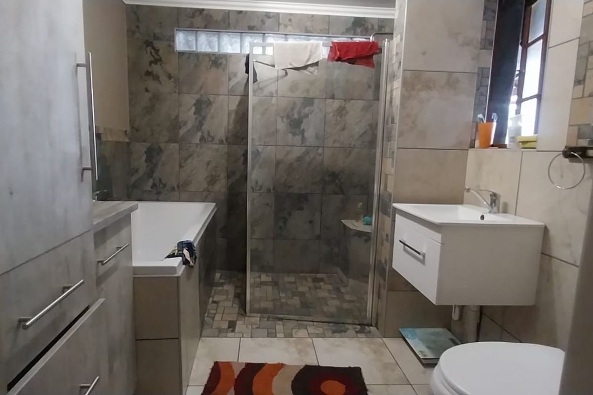A functional bathroom featuring a built-in bathtub, a glass-enclosed shower, a wall-mounted vanity, and tiled wall finishes.
