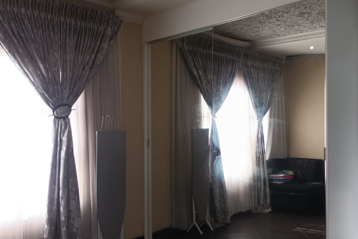Bedroom featuring large mirrored sliding wardrobe doors, tiled flooring, and window treatments.