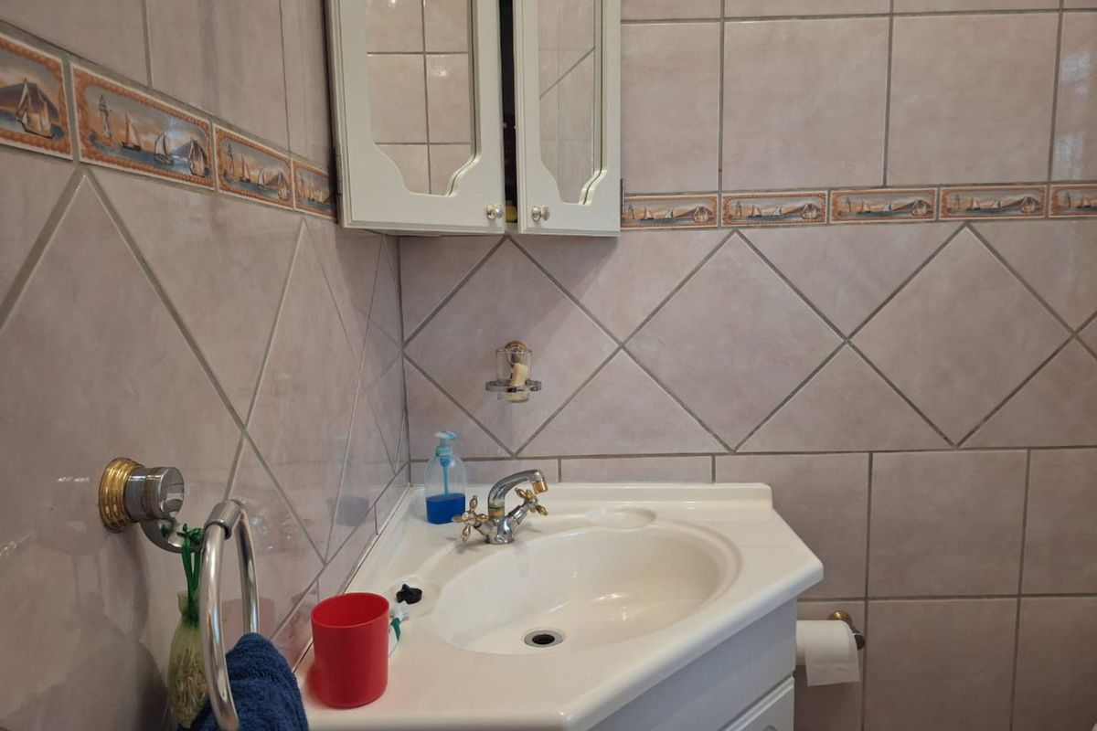 A compact bathroom featuring a corner vanity unit with a basin, wall-mounted mirrored cabinet, and decorative tiled walls.