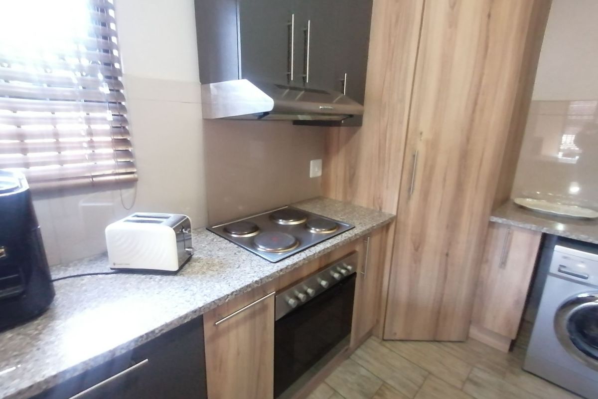 Modern kitchen featuring wood-grain and dark cabinetry, granite countertops, built-in oven, electric hob, extractor fan, and space for a washing machine.
