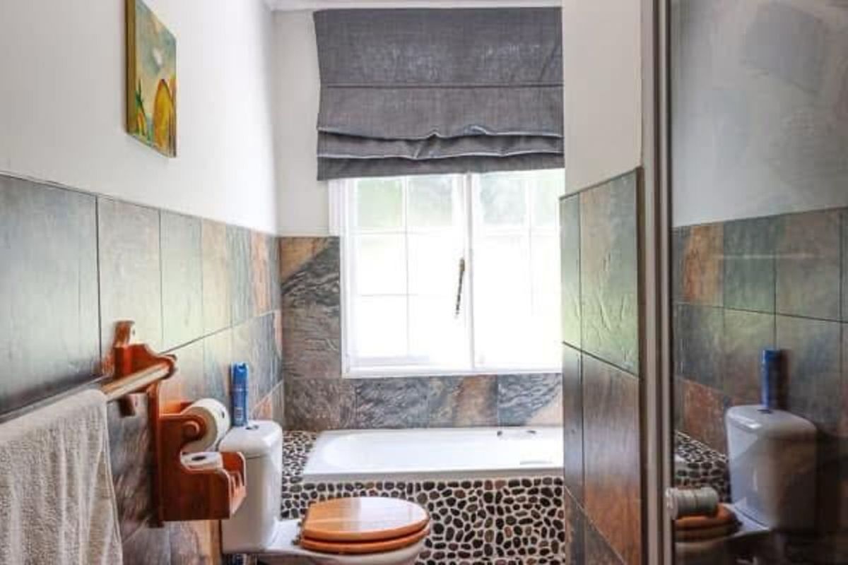 A bathroom featuring a built-in bathtub with pebble-tiled surround, dark slate-style wall tiles, and a standard toilet.