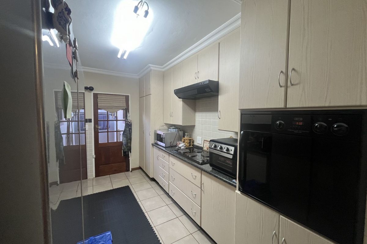 A functional galley-style kitchen featuring light wood-grain cabinetry, a built-in oven, a hob with an extractor fan, and tiled flooring.
