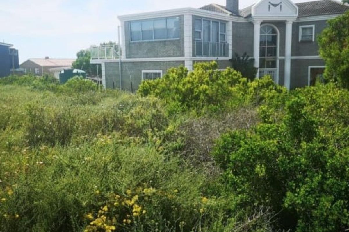 A view of a residential property from an adjacent vacant plot, featuring established landscaping and a multi-story dwelling with architectural detailing.