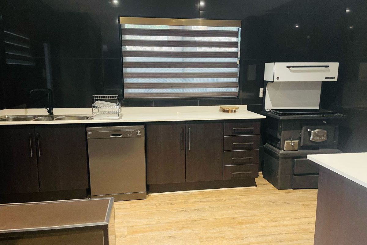 Modern kitchen featuring dark cabinetry, white countertops, a double sink, and a built-in wood-burning stove with an extractor hood.
