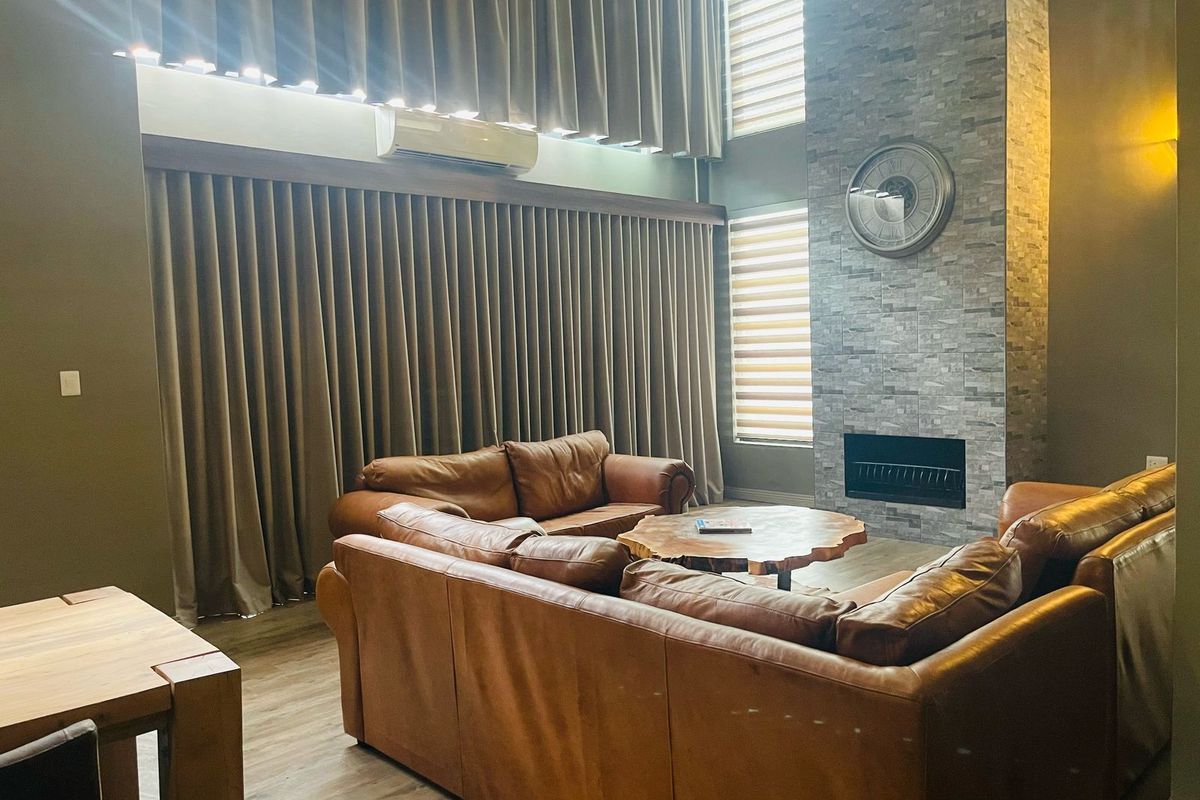 Spacious living area featuring a double-volume ceiling, floor-to-ceiling curtains, a stone-clad fireplace, and modern split-system air conditioning.