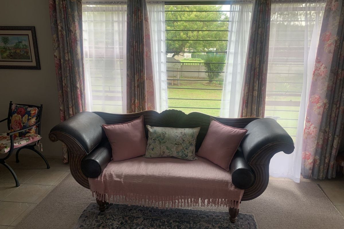 A living room area featuring large windows with security bars, overlooking the garden.