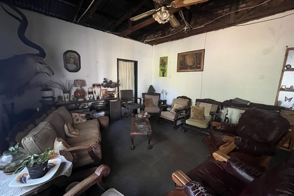 A rustic living room featuring an exposed timber roof structure, ceiling fan, and traditional wall finishes, offering a spacious layout for family gatherings.
