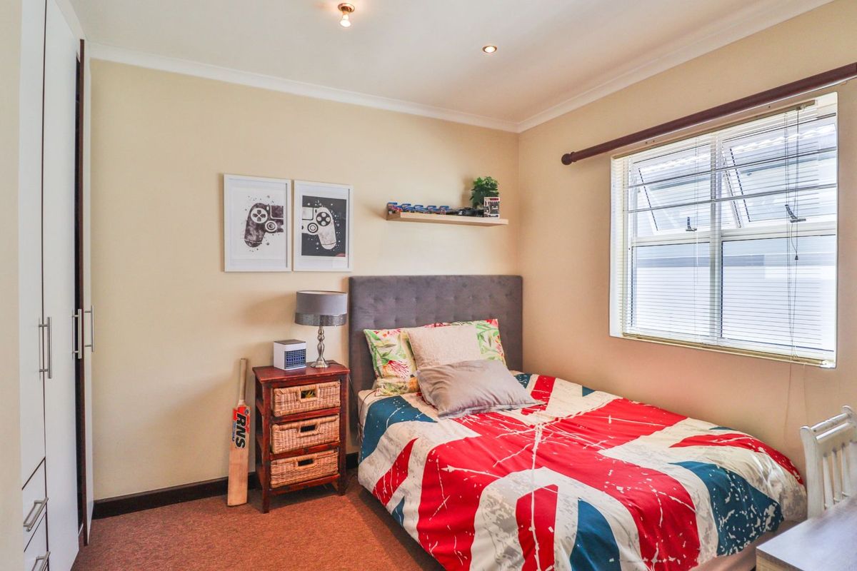 A well-maintained bedroom featuring built-in cupboards, carpeted flooring, and a window with fitted blinds.