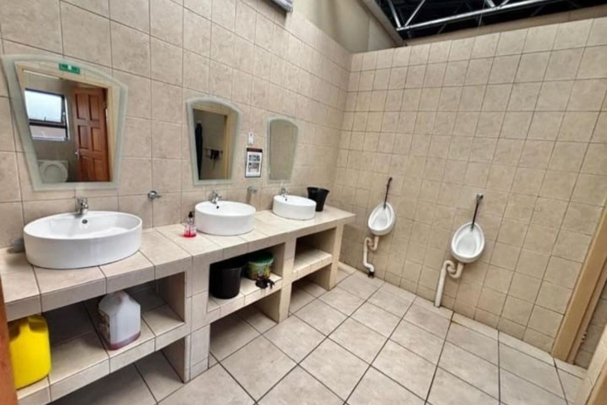 Industrial restroom facility featuring a tiled vanity with three vessel sinks, wall-mounted urinals, and exposed structural ceiling elements.