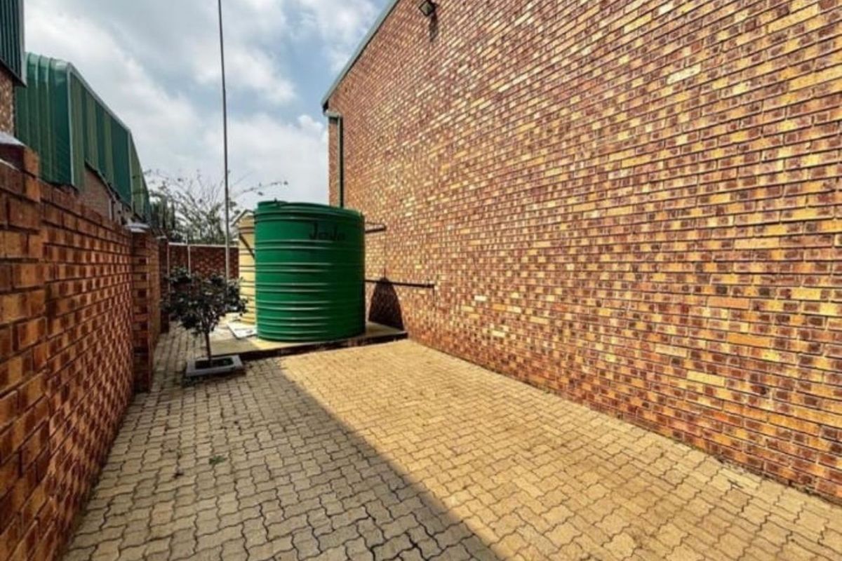 Side exterior area featuring face brick walls, paved ground surface, and a large green water storage tank.