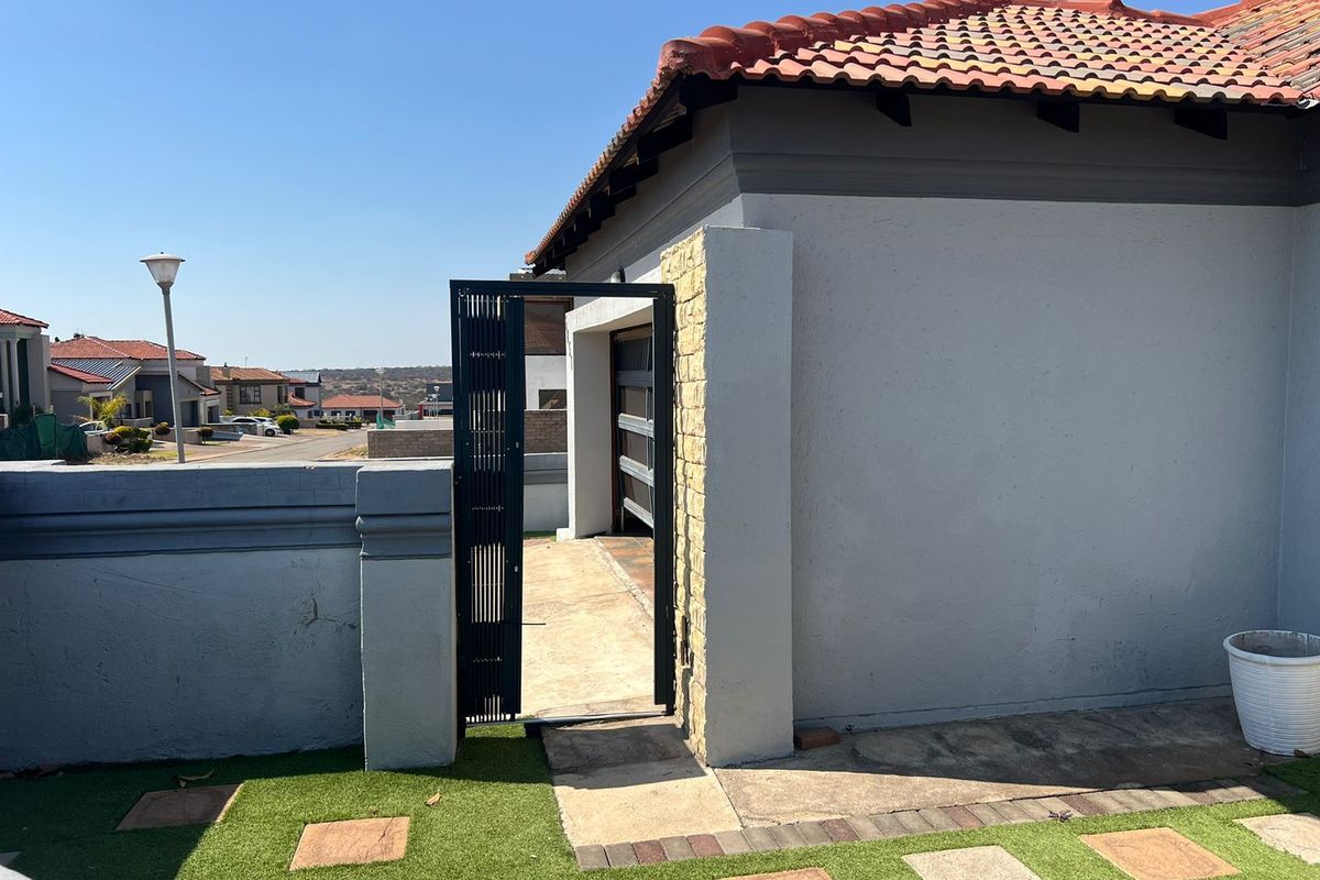 A view of the side exterior area featuring a metal gate, paved walkway, and artificial lawn, leading towards the garage entrance.