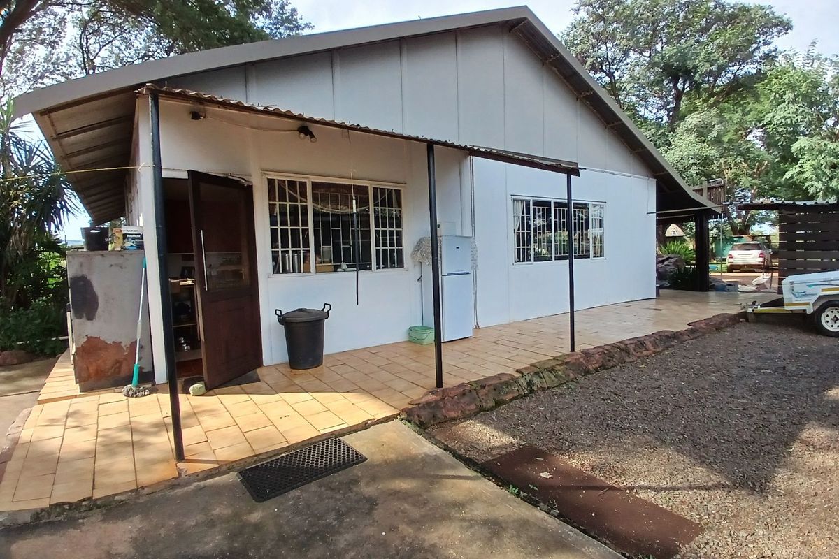 Exterior view of a farm dwelling featuring a covered tiled patio area, metal roof structure, and white exterior walls.
