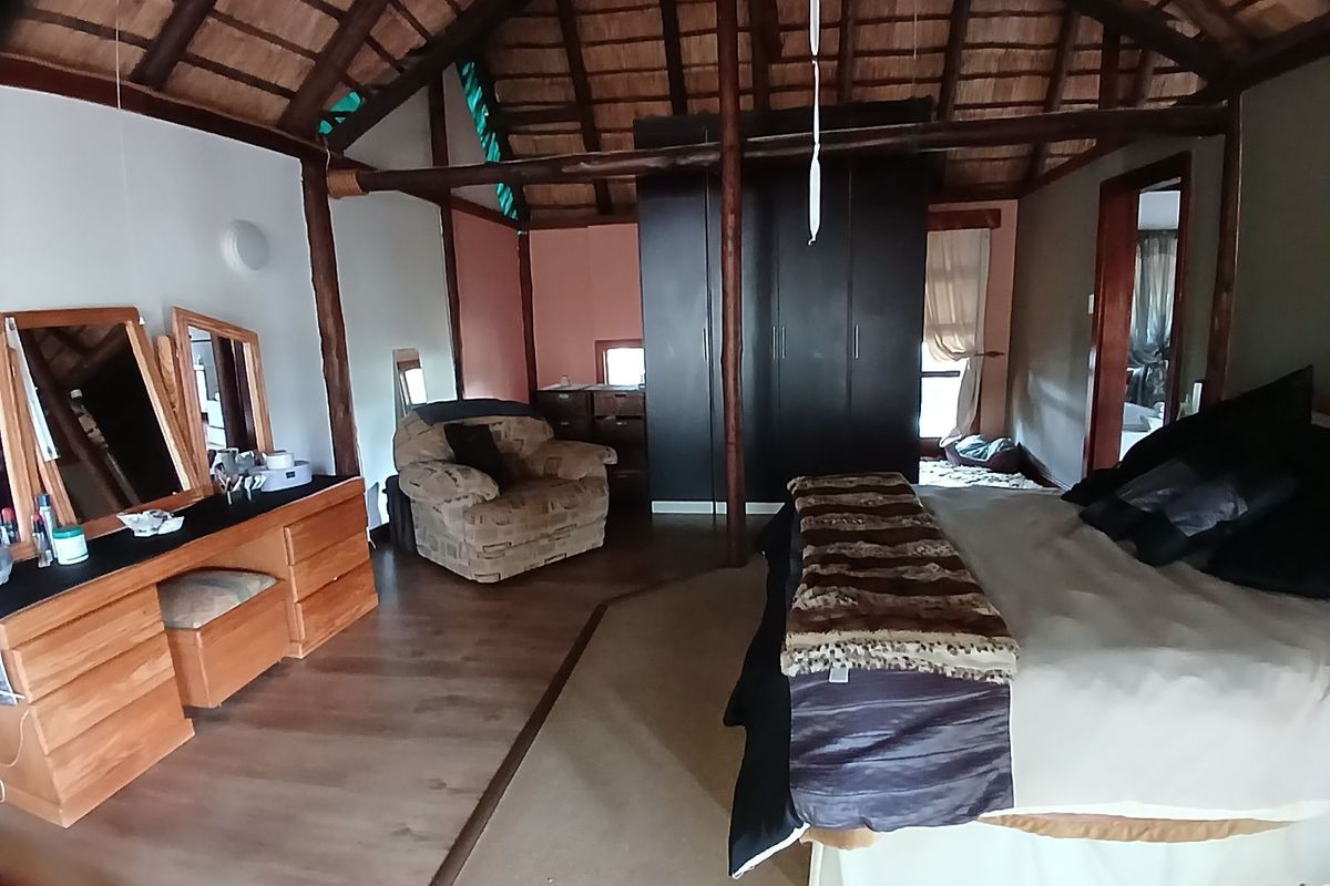 Spacious bedroom featuring a high vaulted thatched roof with exposed timber beams and built-in dark cabinetry.