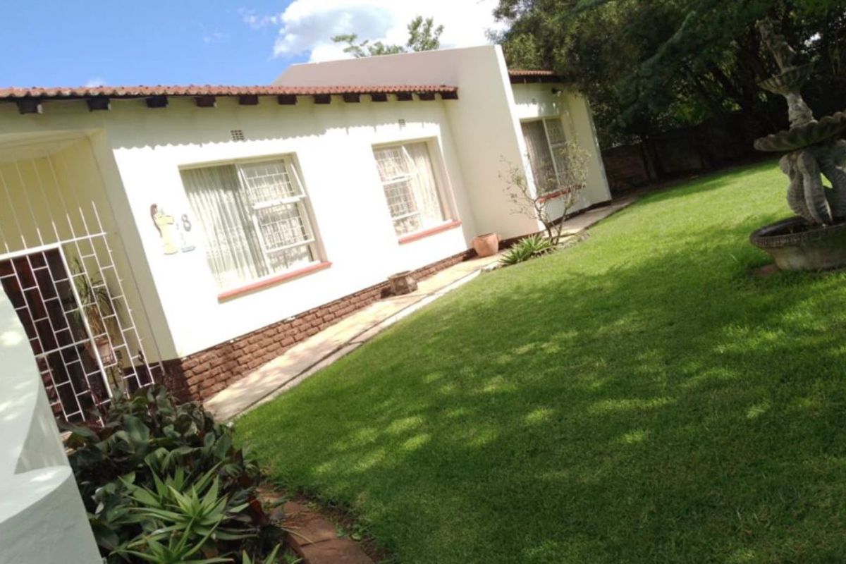 A view of the rear exterior of the house featuring a well-maintained lawn, garden area, and a decorative stone fountain.