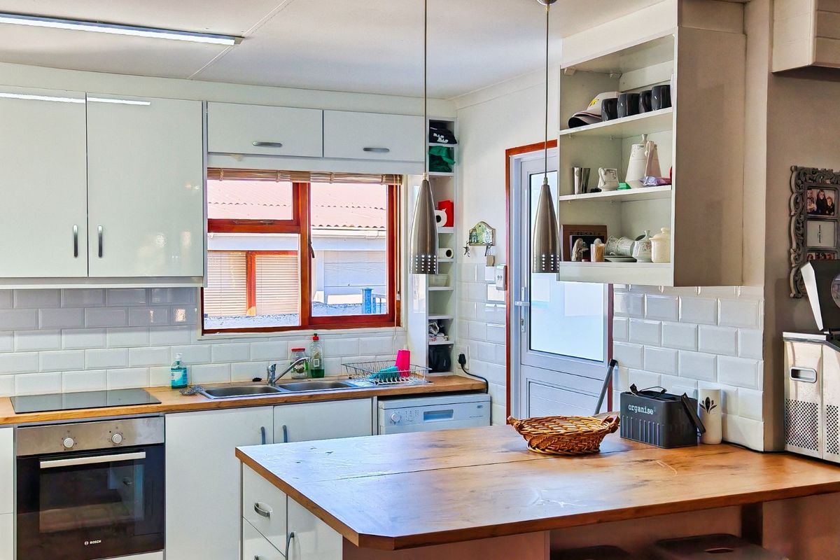 A functional kitchen featuring white cabinetry, subway tile backsplash, timber countertops, built-in oven, and a central island with pendant lighting.