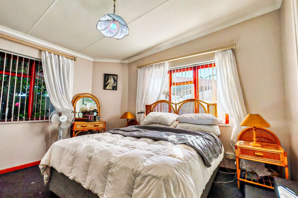 A bedroom featuring carpeted flooring, security bars on windows, and a central ceiling light fixture.