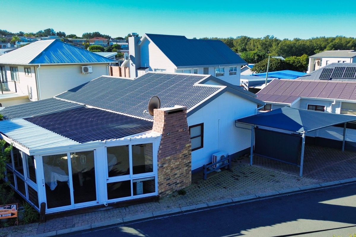 Aerial view of the property featuring a corrugated metal roof, brick chimney, enclosed patio area, and a paved carport.