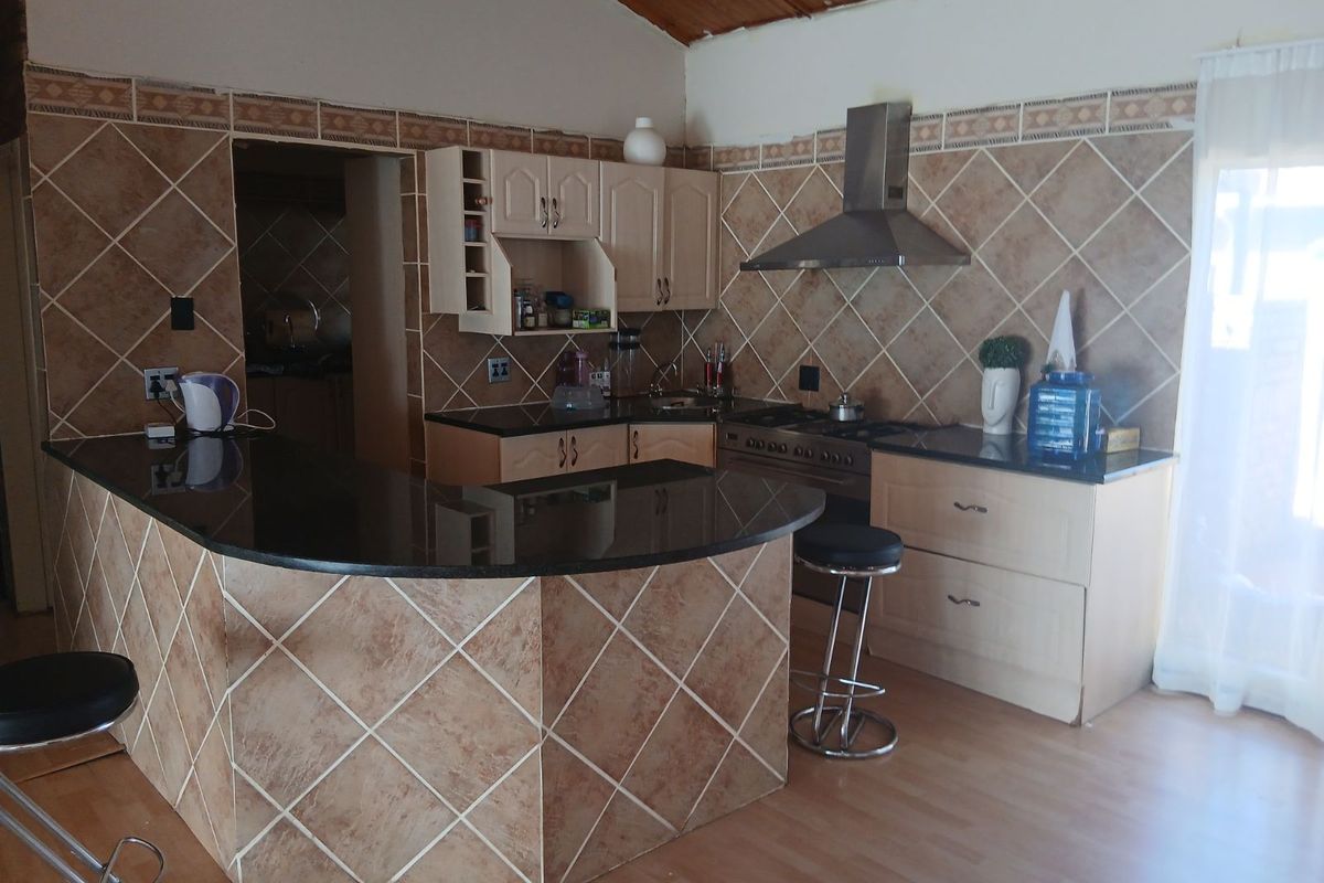 A functional kitchen featuring a breakfast bar, granite countertops, built-in cabinetry, a stainless steel extractor fan, and a gas stove.