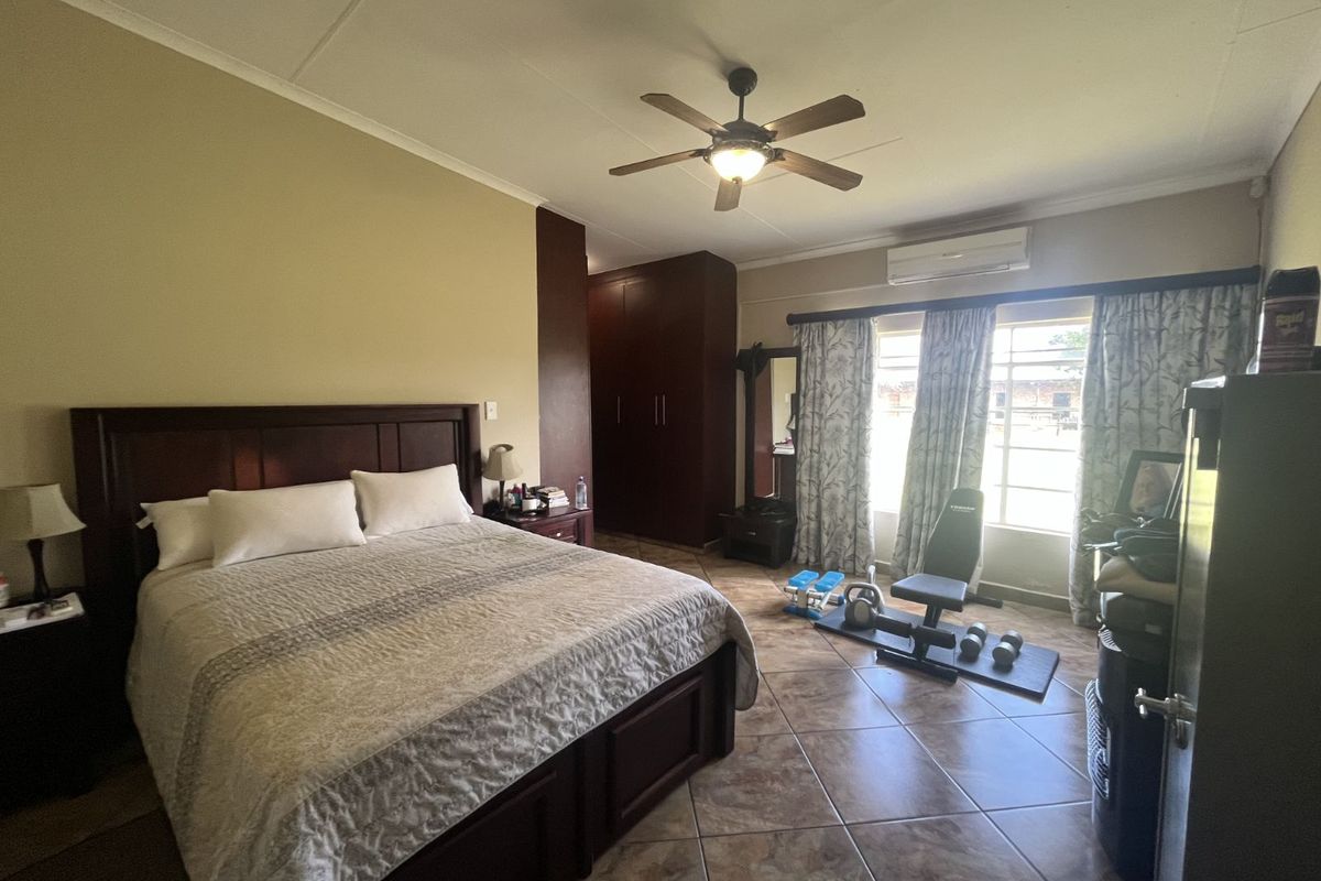 Spacious bedroom featuring tiled flooring, built-in wooden cupboards, a ceiling fan, and a wall-mounted air conditioning unit.